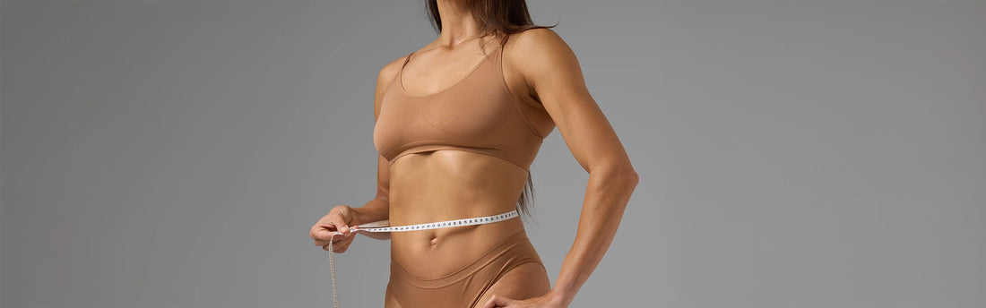 Seitenansicht fitte Frau Taille messen weißes Maßband brauner Fitness Gesundheit